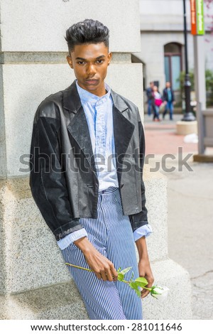 Lonely boy. A 18 years old black student, wearing fashionable jacket, striped pants, blue dyed white shirt, standing by gate on campus, holding white rose, thinking, lost in thought. Retro effect.