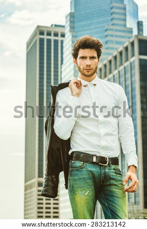 European businessman in New York. Wearing white shirt, holding leather jacket on shoulder, a young guy with beard, standing in front of business district, confidently looking forward. Instagram effect