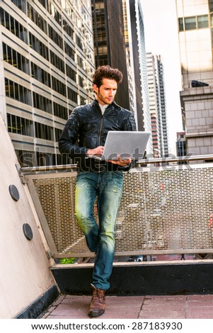 European businessman working in New York. Wearing leather jacket, jeans, boot shoes, a guy with beard, standing by railing in business district, working on laptop computer. Instagram filtered effect.
