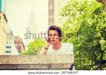 European college student traveling in New York. Wearing white T shirt, a young guy calling on his mobile phone outside on street in summer. Technology in our daily life. Instagram filtered effect.