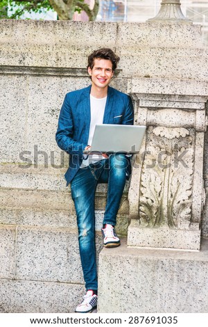 European college student studying in New York. Wearing blue blazer, jeans, sneakers, a young guy staying at quiet corner on campus, working on laptop computer, reading, thinking. Working Outside.