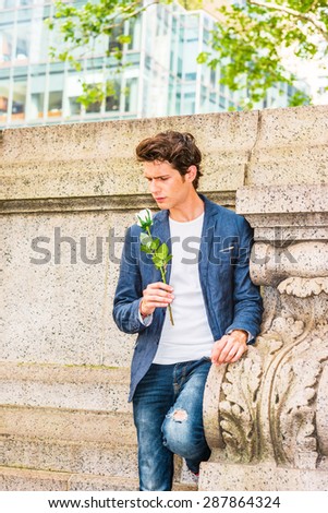 European college student seeking love in New York. Wearing blue blazer, jeans, a young guy standing at corner against wall on campus, holding white rose, thinking, missing you. Instagram effect.