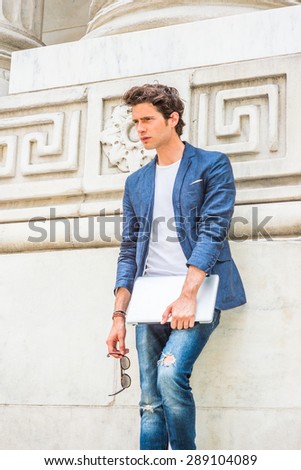 European college student studying in New York. Wearing blue blazer, white under shirt, jeans, holding laptop computer, sunglasses, a young guy standing by column on campus, relaxing. thinking.