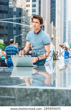 European college student study in New York. Wearing blue pattered shirt, holding glasses, a young handsome guy working on laptop computer on street, looking up, thinking. Many people on background.