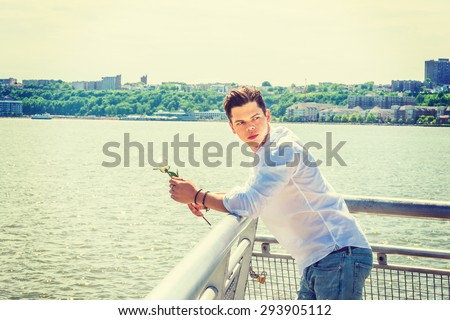 Man Missing You. Wearing white shirt, jeans, holding white rose, a young guy standing by Hudson River in New York, crossing New Jersey, head turning back, waiting for you. Instagram effect. Copy Space
