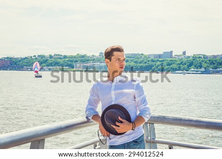 Man Waiting You for sailing. Wearing white shirt, holding Fedora hat, sunglasses, a guy standing by Hudson River in New York, opposite New Jersey, turning back, looking forward. A boat on background.