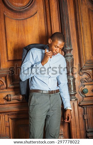 African American businessman working in New York. Wearing striped shirt, hand hooking jacket on shoulder, a black teacher standing by vintage style library door way, lowering head, tired, thinking.