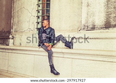 Man seeking love in New York. Wearing black leather jacket, jeans, boots, hand holding white rose, a young black guy sitting against wall with window on street, looking back, waiting for you.