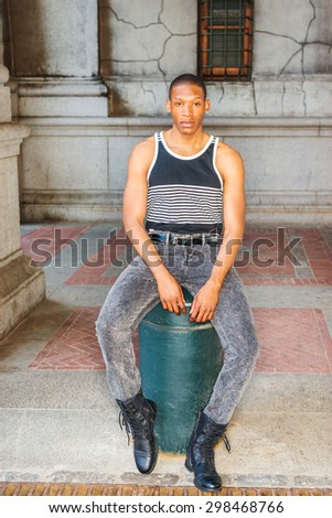 Man casual street fashion. Wearing black, white striped tank top, jeans, leather boots, a young African American guy sitting on street in New York, relaxing, thinking, lost in thought.
