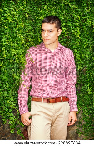 Love Green. Portrait of Student. Wearing red patterned, long sleeve shirt, yellow pants, a young guy standing against wall with long green leaves, smiling, Concept of Environment Protection.