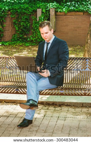 Businessman traveling, working in New York. Dressing in black suit, tie, gray pants, leather shoes,  a young guy sitting on metal chair on street, reading, working on laptop computer. Way to success.