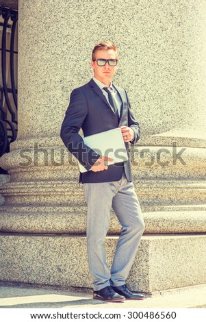 Lawyer. Dressing in black blazer, tie, gray pants, leather shoe, wearing mirror sunglasses, holding laptop computer, a businessman standing by column, confidently looking forward. Instagram effect.