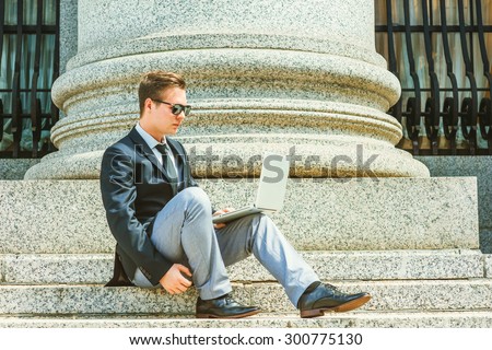 Businessman working under sunshine in New York. Dressing in black blazer, tie, gray pants, leather shoes, wearing sunglasses, a lawyer sitting on stairs outside, reading, working on laptop computer.