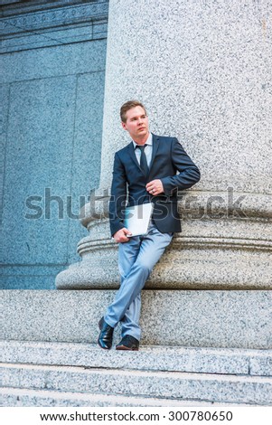 Thinking outside. Dressing in black blazer, tie, gray pants, leather shoe, holding laptop computer, crossing legs, a businessman standing against column outside office, taking break during work.