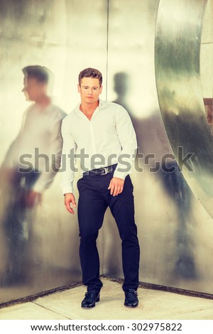 Man casual fashion. Wearing white shirt, black pants, leather shoes, a young, strong, sexy guy casually standing against silver metal wall, taking break during work. Instagram filtered effect.
