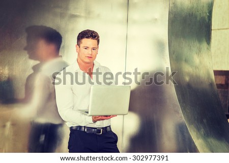 American Businessman working outside. Wearing white shirt, black pants, a young, strong, sexy guy standing by silver metal wall, holding laptop computer, reading, thinking. Instagram filtered effect.