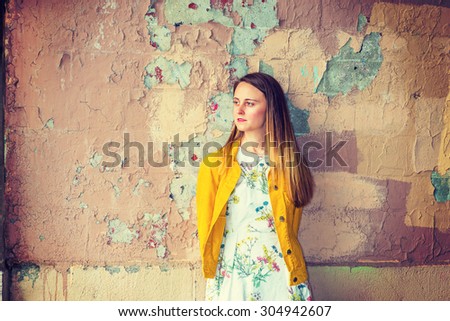 I missing you, waiting you in old place. A pretty American girl wearing flower patterned underdress, yellow corduroy jacket, standing by wall peeling off paints, looking away. Instagram effect.
