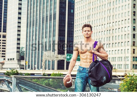 Play Hard, Work Smart. Shirtless, half naked, waring jeans, a young, strong, sexy guy, carrying big duffel bag, holding football, walking from business district in New York, going to play field.