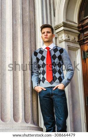 American College Student Studying in New York. Wearing black, white, gray patterned sweater, red necktie, jeans, a young man standing outside vintage style office, thinking, lost in thought.