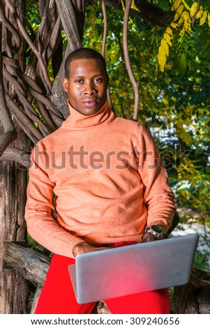 Technology in our daily life. Dressing in light orange knit sweater with high collar, red pants, an African American guy sitting by trees in New York in autumn, working on laptop computer, thinking.