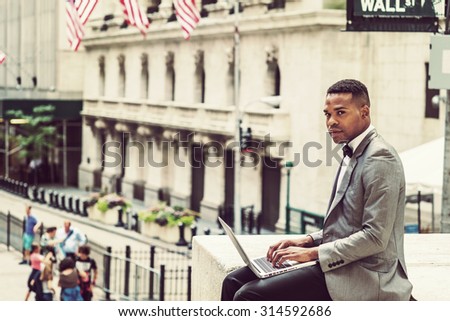 African American Businessman working in New York. Wearing gray blazer, bow tie, young black man siting on Wall Street, reading, working on laptop computer, looking around, thinking. Instagram effect.