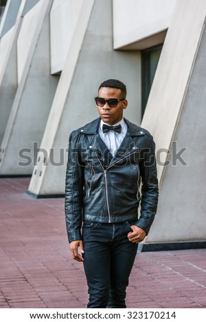 Man Urban Autumn/Spring Casual Fashion. Wearing black leather jacket, black jeans, sunglasses, white undershirt, black bow tie, a young African American guy walking on street in New York. City Boy.