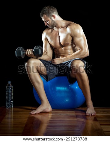 Young adult man drinking protein shake in gym. Black background.