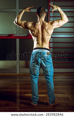 Young adult man showing back of body while posing in gym