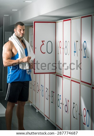 Young adult fit man standing in locker room and opening locker door.