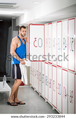 Young adult fit man standing in locker room and opening locker door.