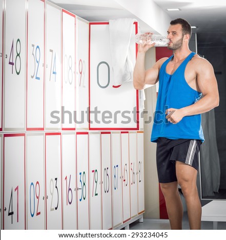 Young fit adult man drinking water in locker room of gym facility.