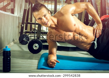 Young teenage guy doing side plank exercise in gym.