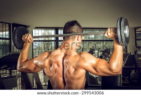 Young teenage man doing weighnt lifting with barbell. View from back.