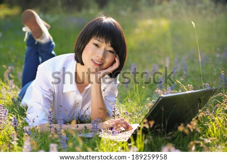 Beautiful asian student using laptop among flowers . Outdoor work and study