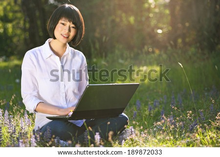 Smiling chinese girl with laptop at the park . Outdoor work and study