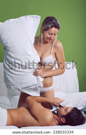Smiling woman playing with pillows in bed with her man. Funny concept