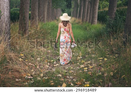 Beautiful woman with flowered dress walking in a meadow with trees