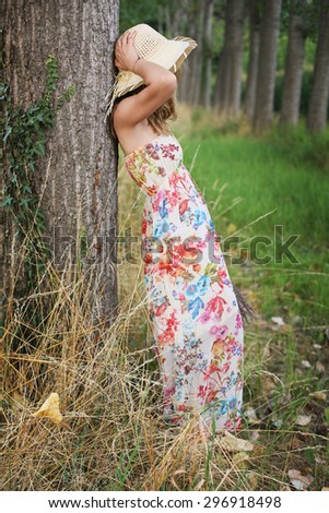 Young woman with flower dress leaning to a tree . Country and nature portrait