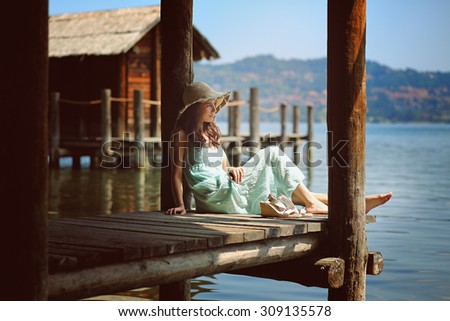 Beautiful young woman relaxing close to waters . Wood cabin and lake as background