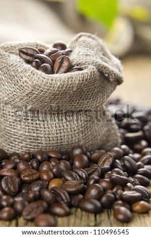 Black roasted coffee beans in a small burlap sack