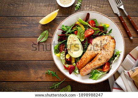 Salmon fish steak grilled, avocado and fresh vegetable salad with tomato, bell pepper and leafy vegetables. Top view, copy space.