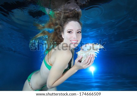 Beautiful woman smiling underwater in the pool with sea shell