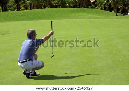 Golfer sitting down on the green, lining up the putter.