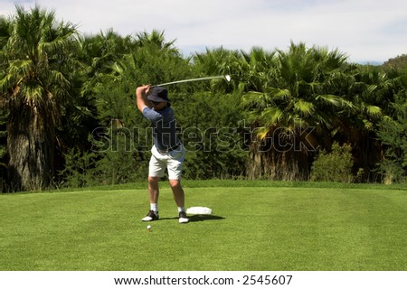 Golfer hitting the ball from the tee box. Golf club is in motion.