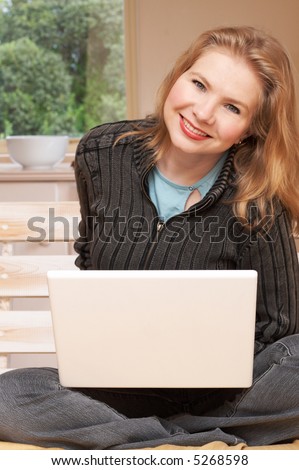 Blonde woman in casual clothes sitting  on the couch and working on her laptop