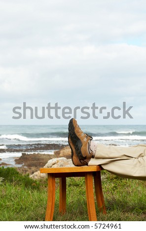 Man resting his feet on top of the little chair by the ocean