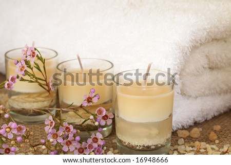 Relaxing spa scene with a white rolled up towel, pink flowers, beautiful handmade candles and bath salts