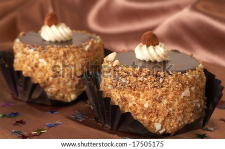 Two miniature chocolate meringue cakes with cream and almonds on golden silk background with  stars scattered. Focus is on the front cake