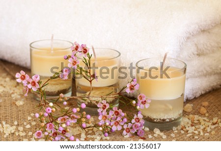 Relaxing spa scene with a white rolled up towel, small pink flowers, beautiful handmade candles and bath salts