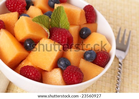 Bowl of summer fruit salad with raspberries, melon, blueberries and mint leaves in white bowl